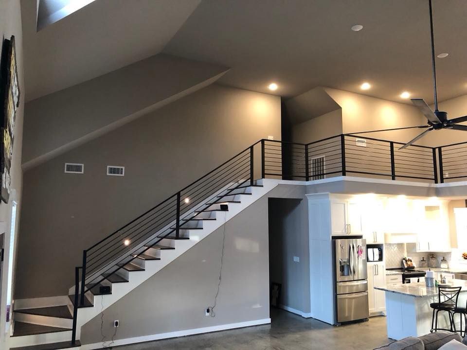 Staircase with black railing and loft overlooking kitchen. Gray walls, modern interior.