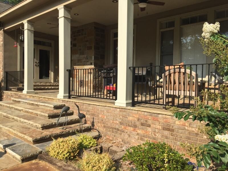 Covered porch with stone steps, black railings, white columns, and outdoor furniture.
