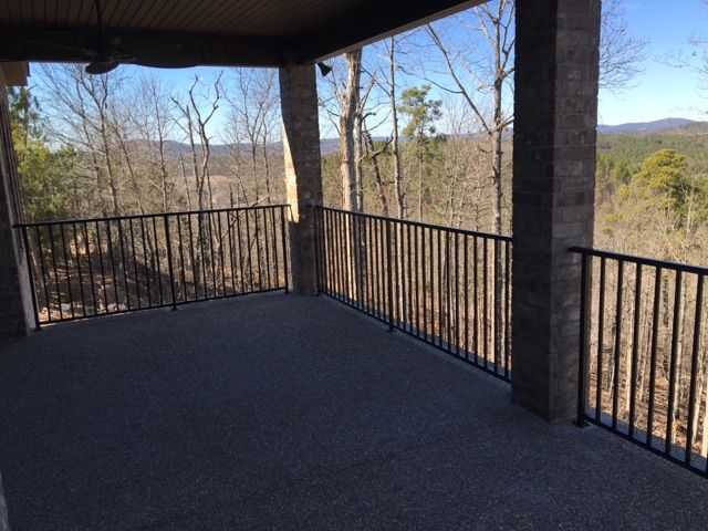 A covered patio with a black railing overlooks a wooded landscape and distant mountains on a sunny day.
