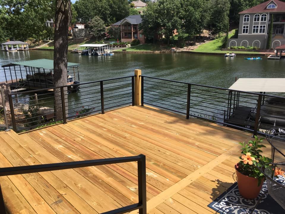 Wooden deck overlooking a lake, with black railings. Boats and houses in the background. Sunny day.