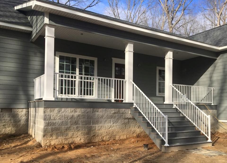Exterior view of a house with a gray facade, white porch railings, steps, and a brown door.