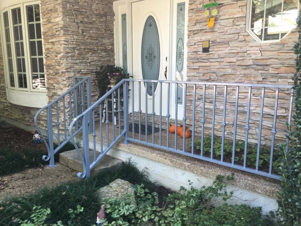 Gray metal railing in front of a stone-faced house entrance with a white door.