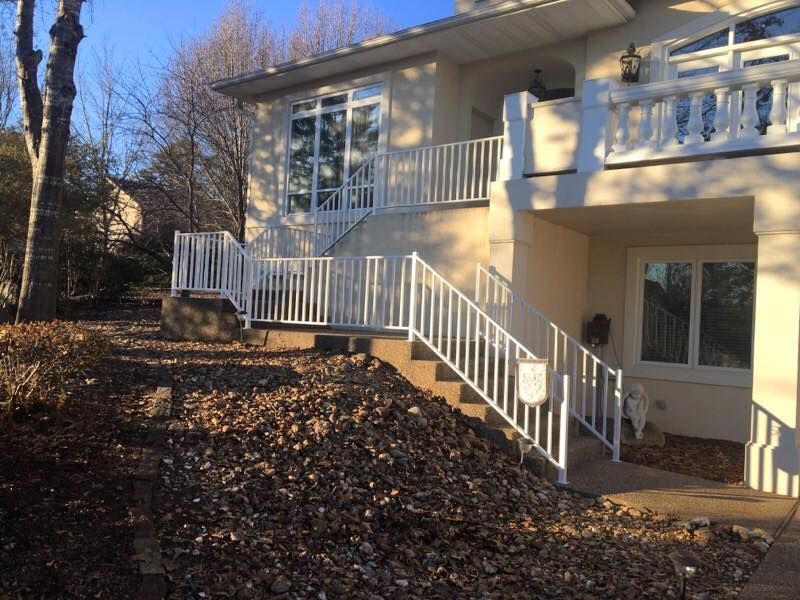 White railing and steps leading up to a two-story beige house on a hill covered in mulch.