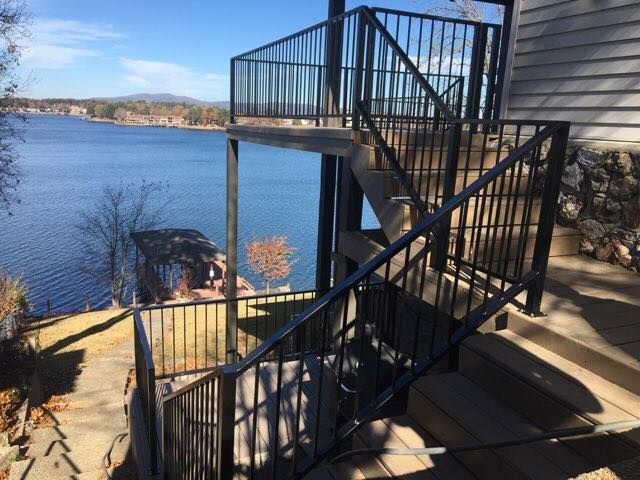 Black metal staircase leads down to a lakefront dock; water and trees in the background.