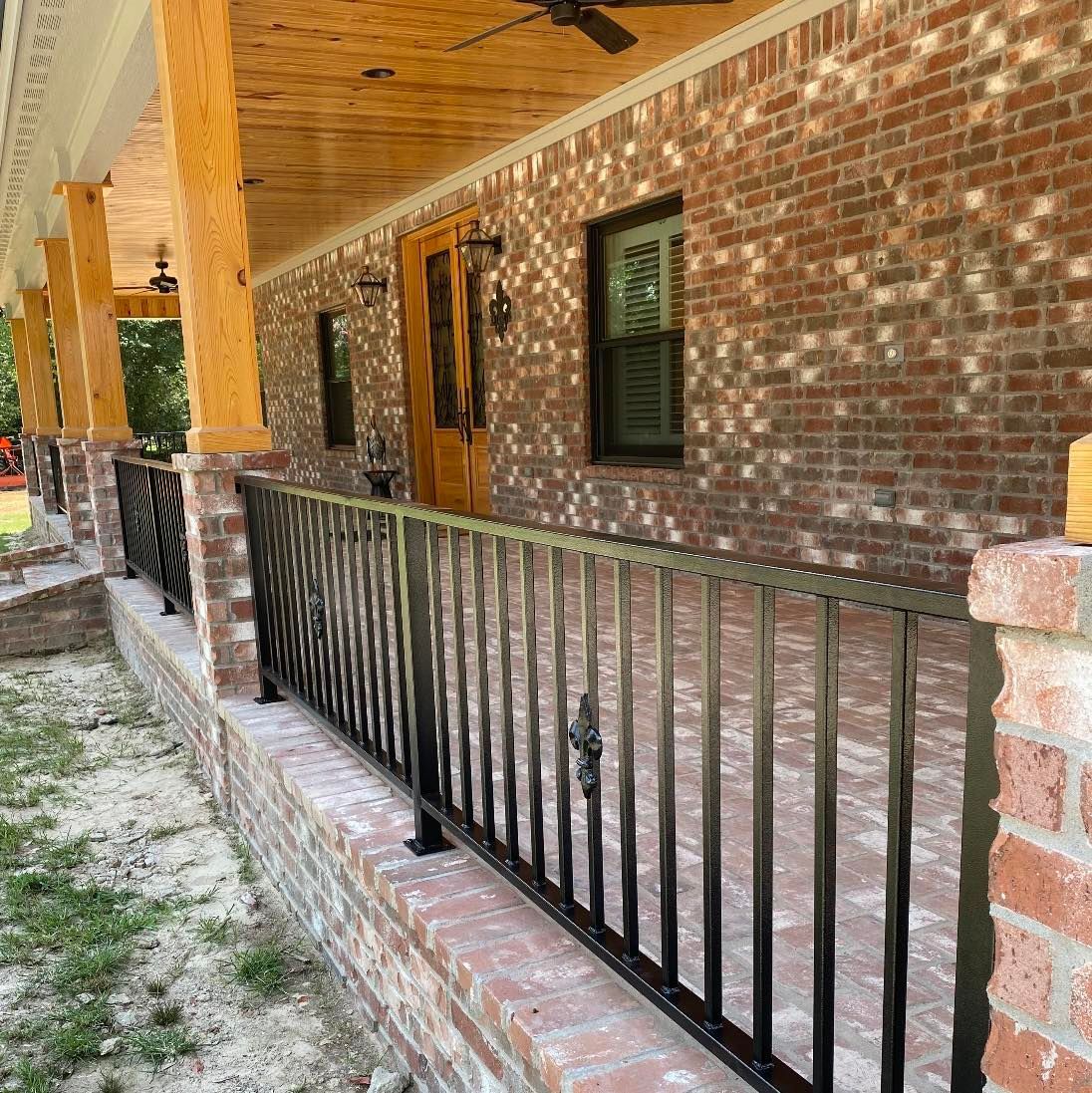 Brick porch with black metal railing, wooden posts, and a wood door.