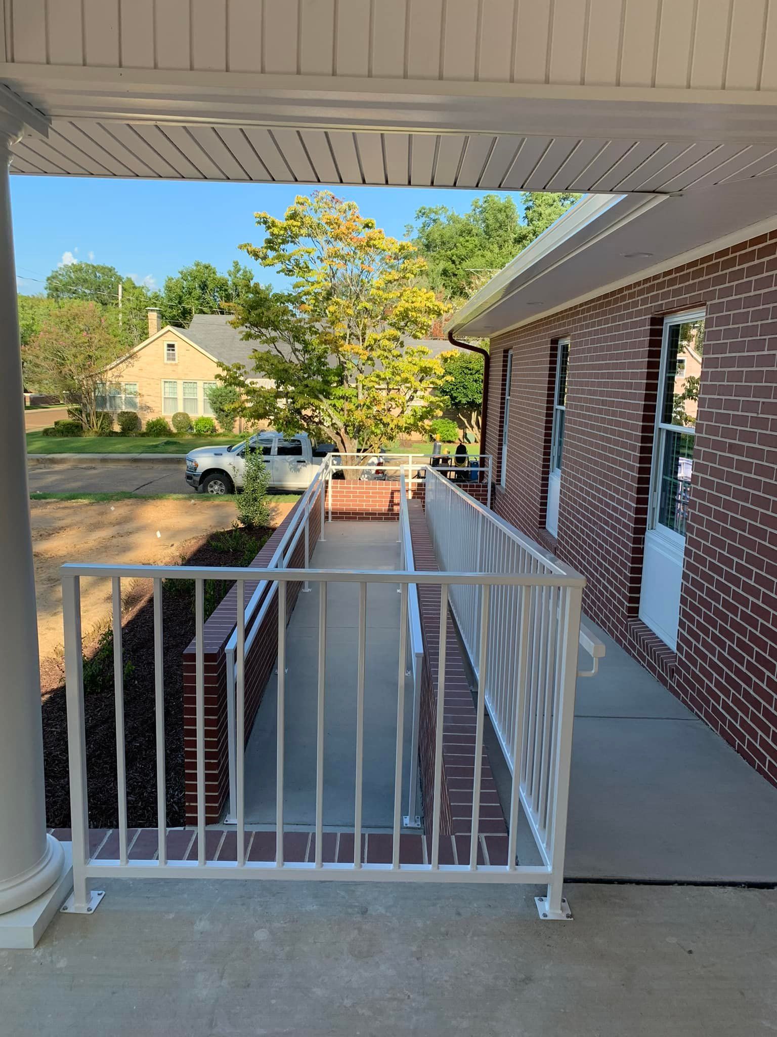 Brick building with a white wheelchair ramp, railing, and a small tree in view.