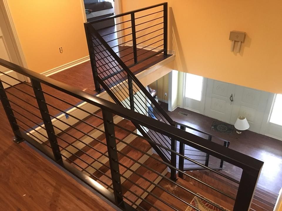Interior view of a staircase with black metal railings and horizontal bars. Wooden floors and peach-colored walls.