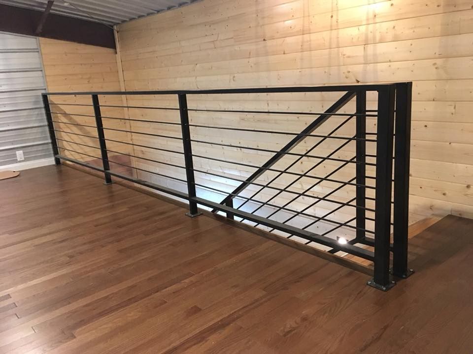 Black metal railing with horizontal bars on a wooden loft overlooking a wood-paneled wall.