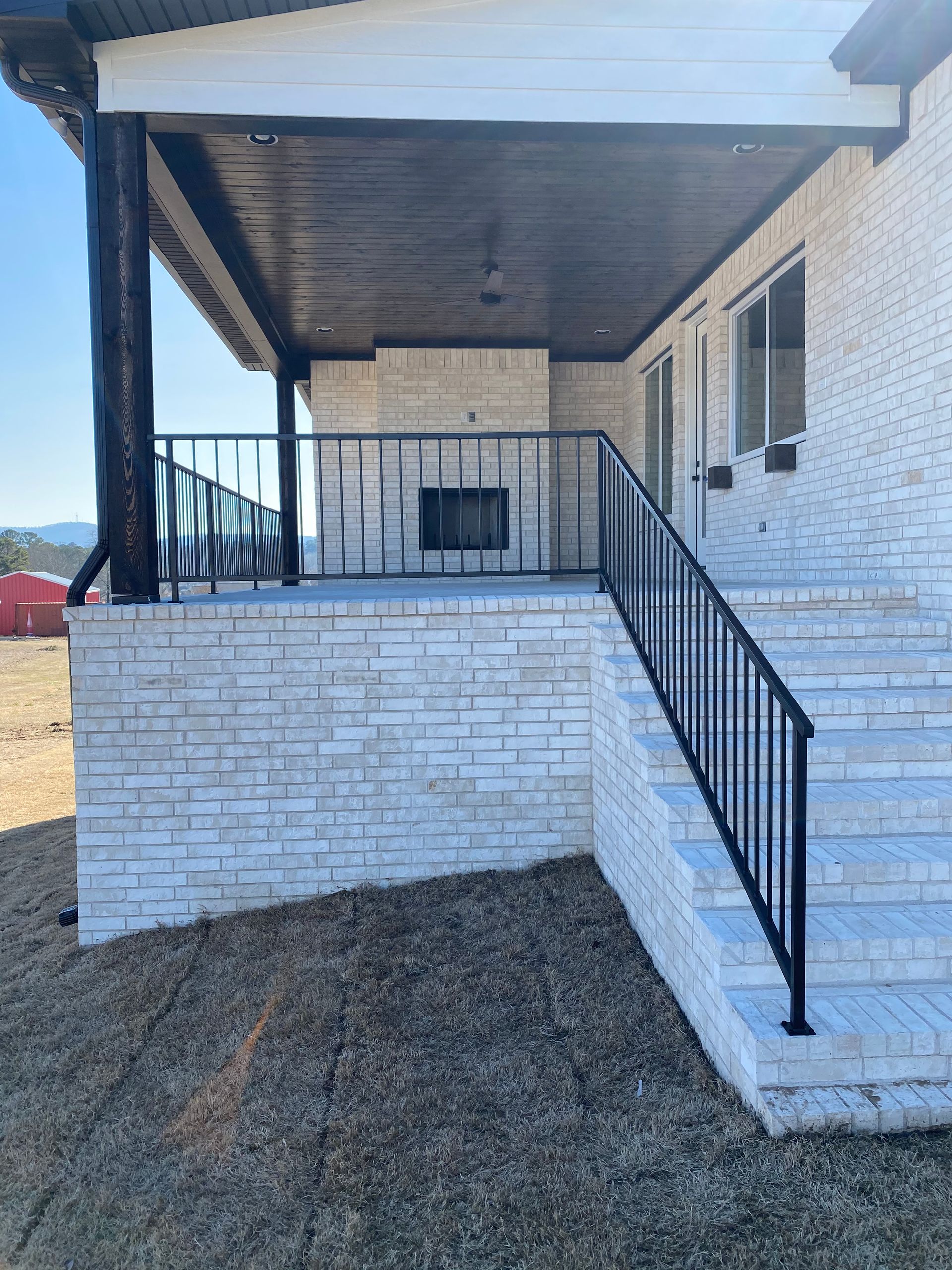Brick porch with black railing and steps on a white house under a covered roof