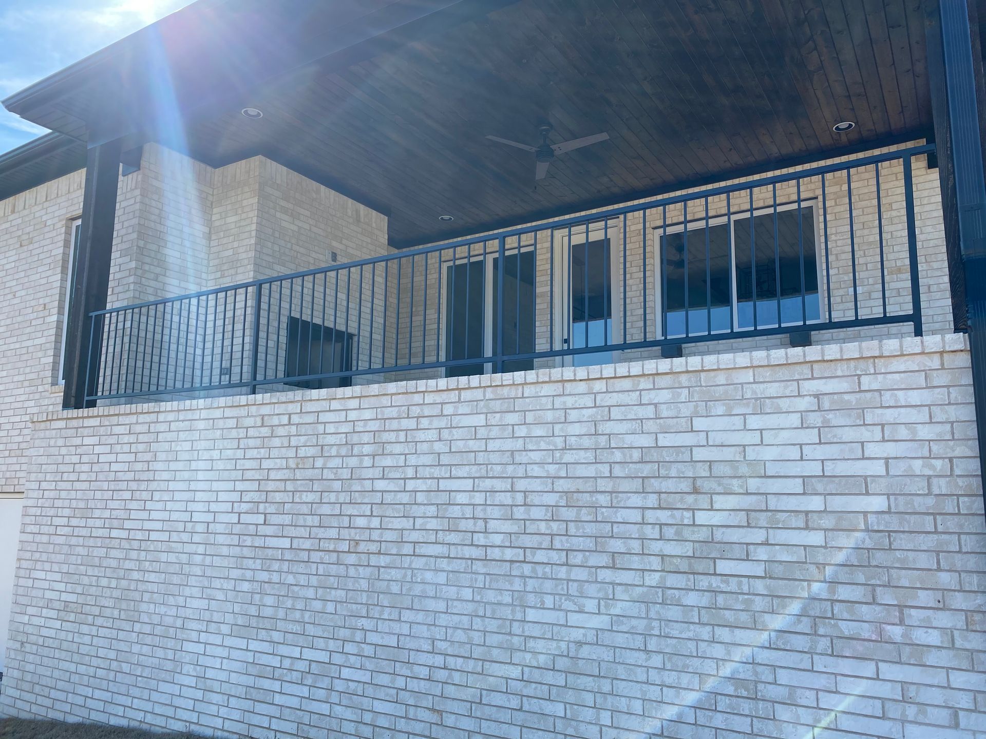 Stone house porch with metal railing and white brick wall in bright sunlight