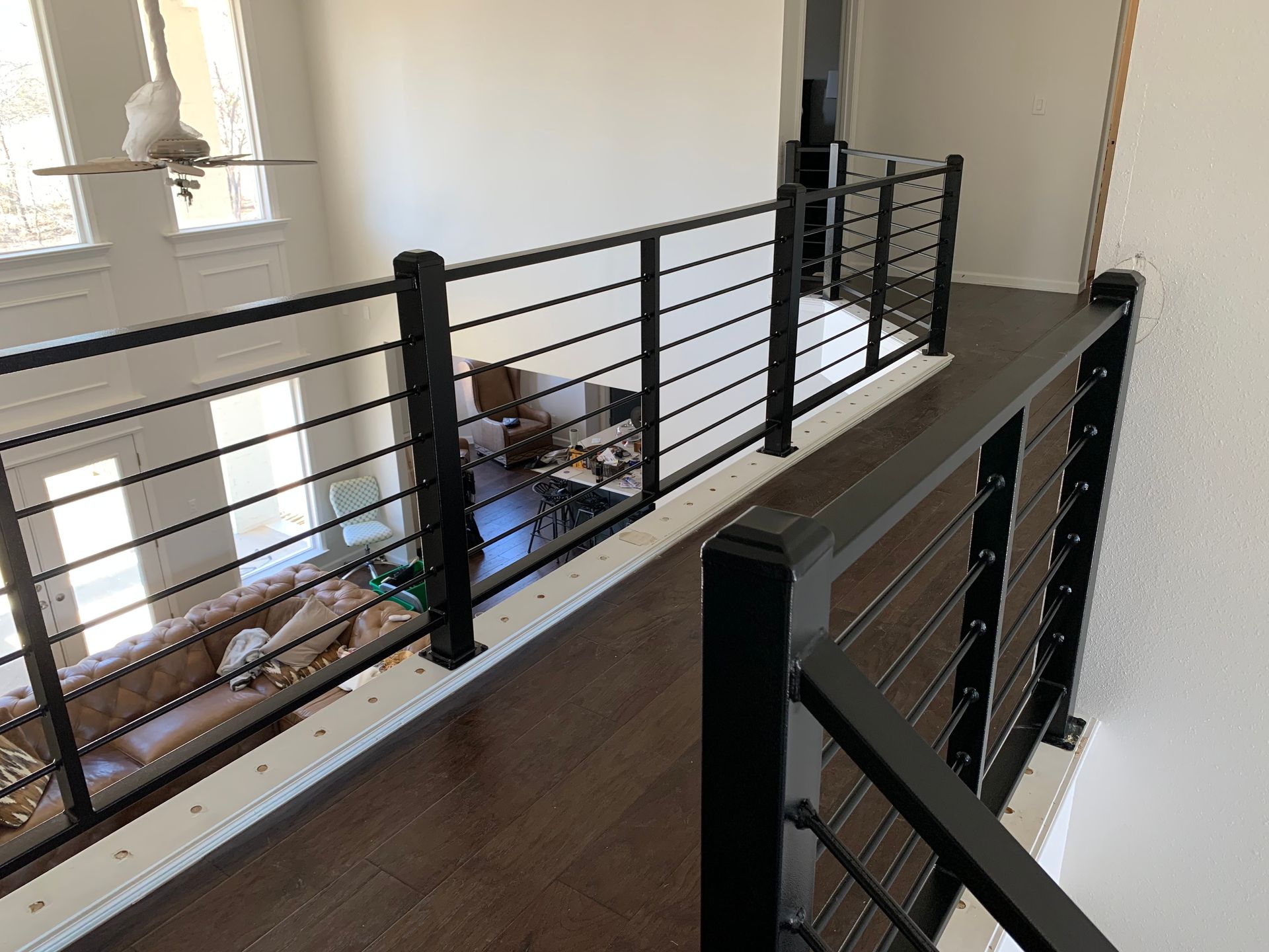 Black cable railing on a wooden second-story walkway overlooking a living room with a couch.