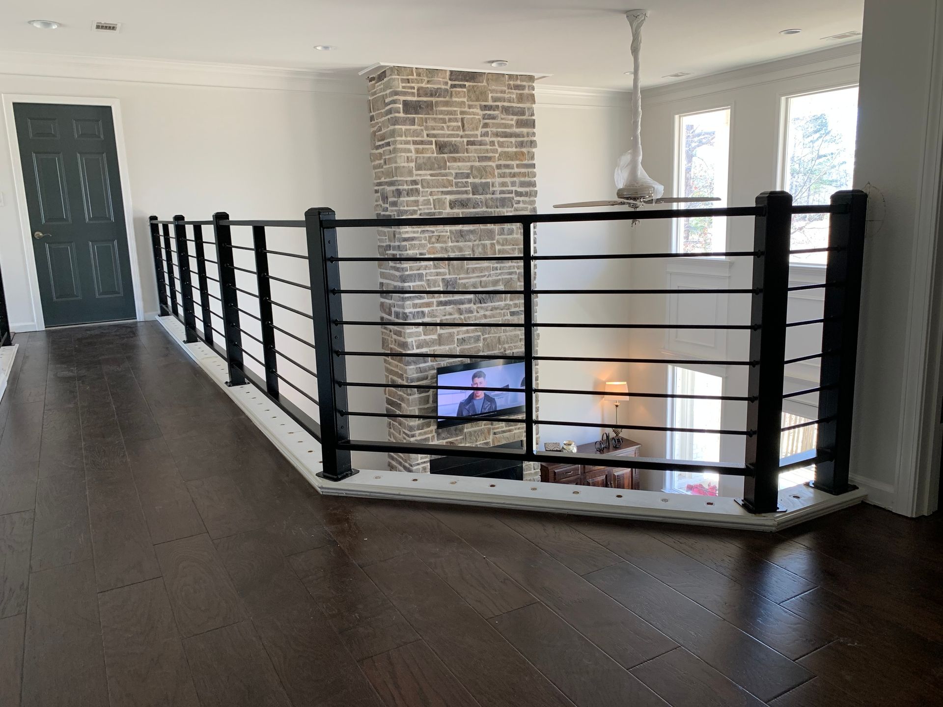 Interior view of a balcony railing with black vertical bars. Dark wood floors and a stone fireplace are visible.