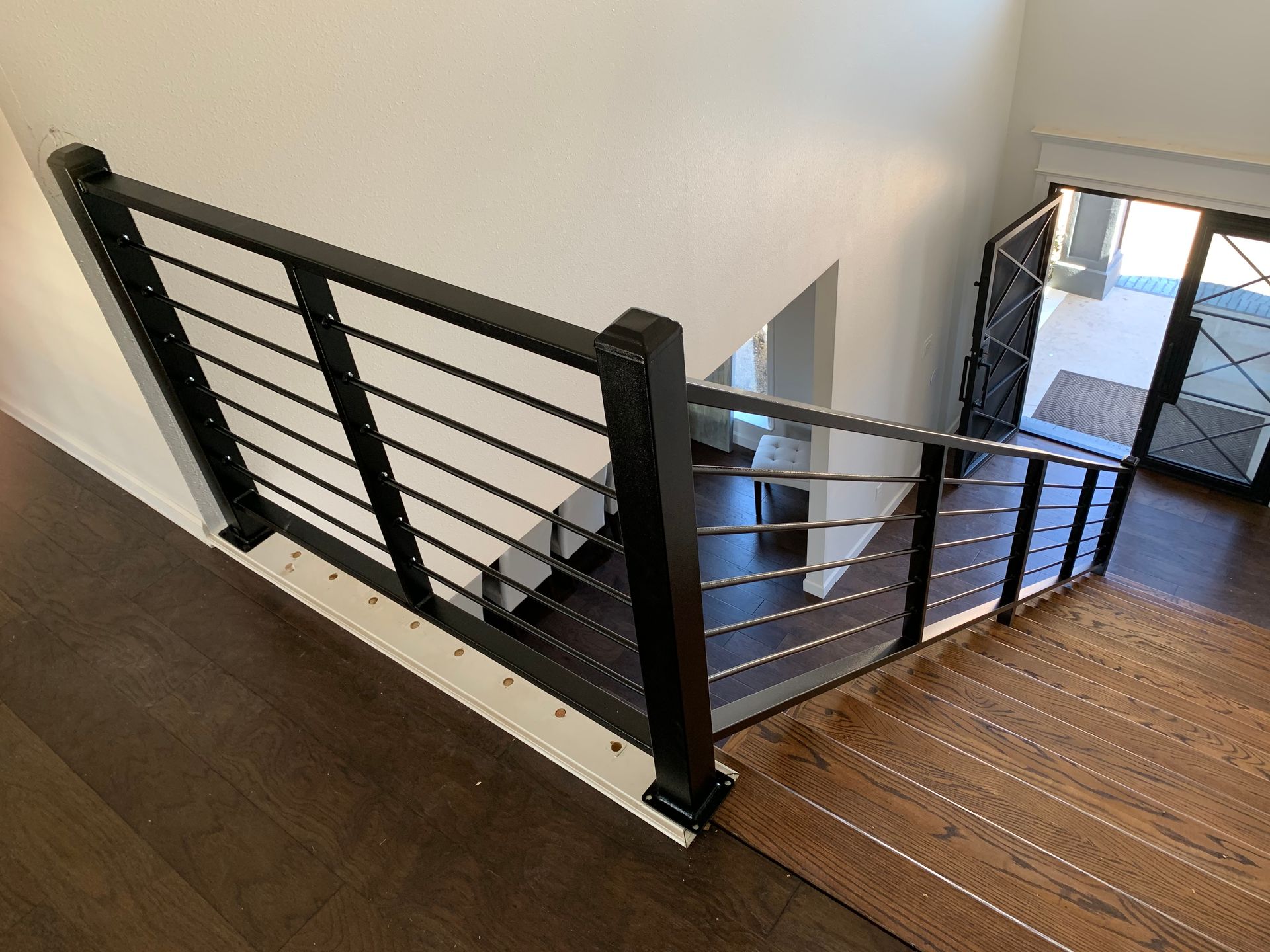 Black metal railing with horizontal bars on a staircase. Dark wood floor and white walls.