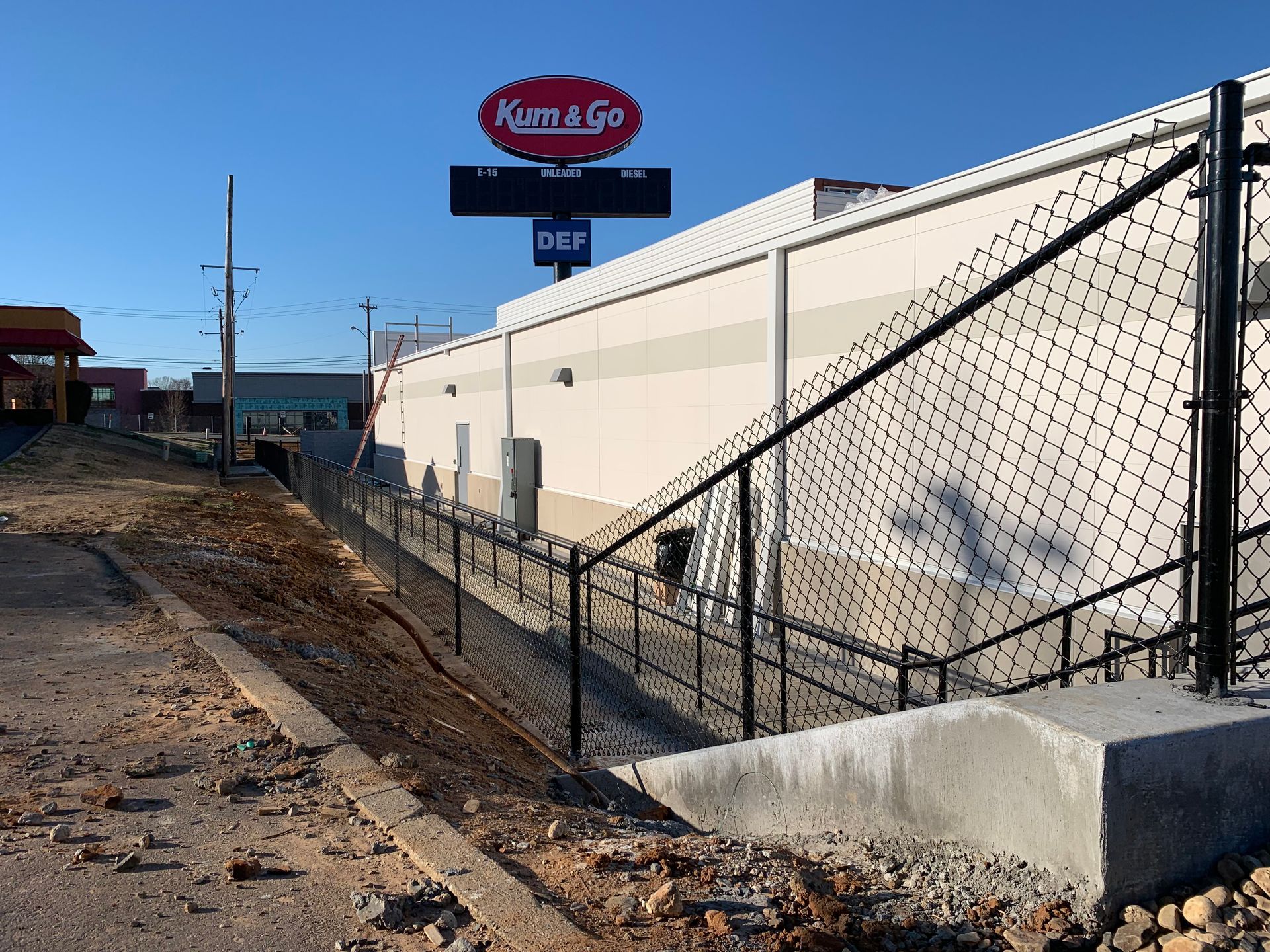 Kum & Go store exterior with a chain-link fence, stairs, and a dirt incline.