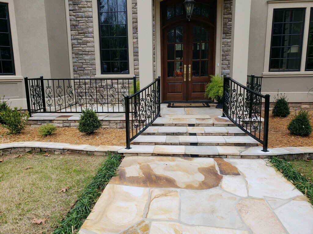 Stone walkway leading to a house with steps and black wrought iron railings.