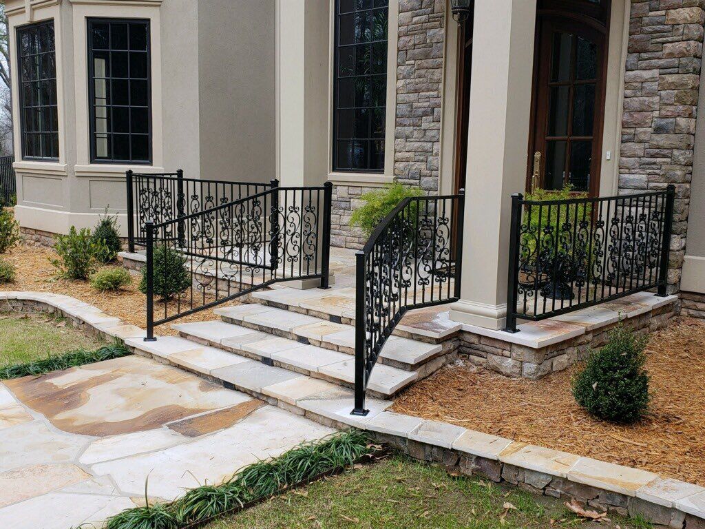 Black metal railings on stone steps leading to a house with a stone and tan exterior.