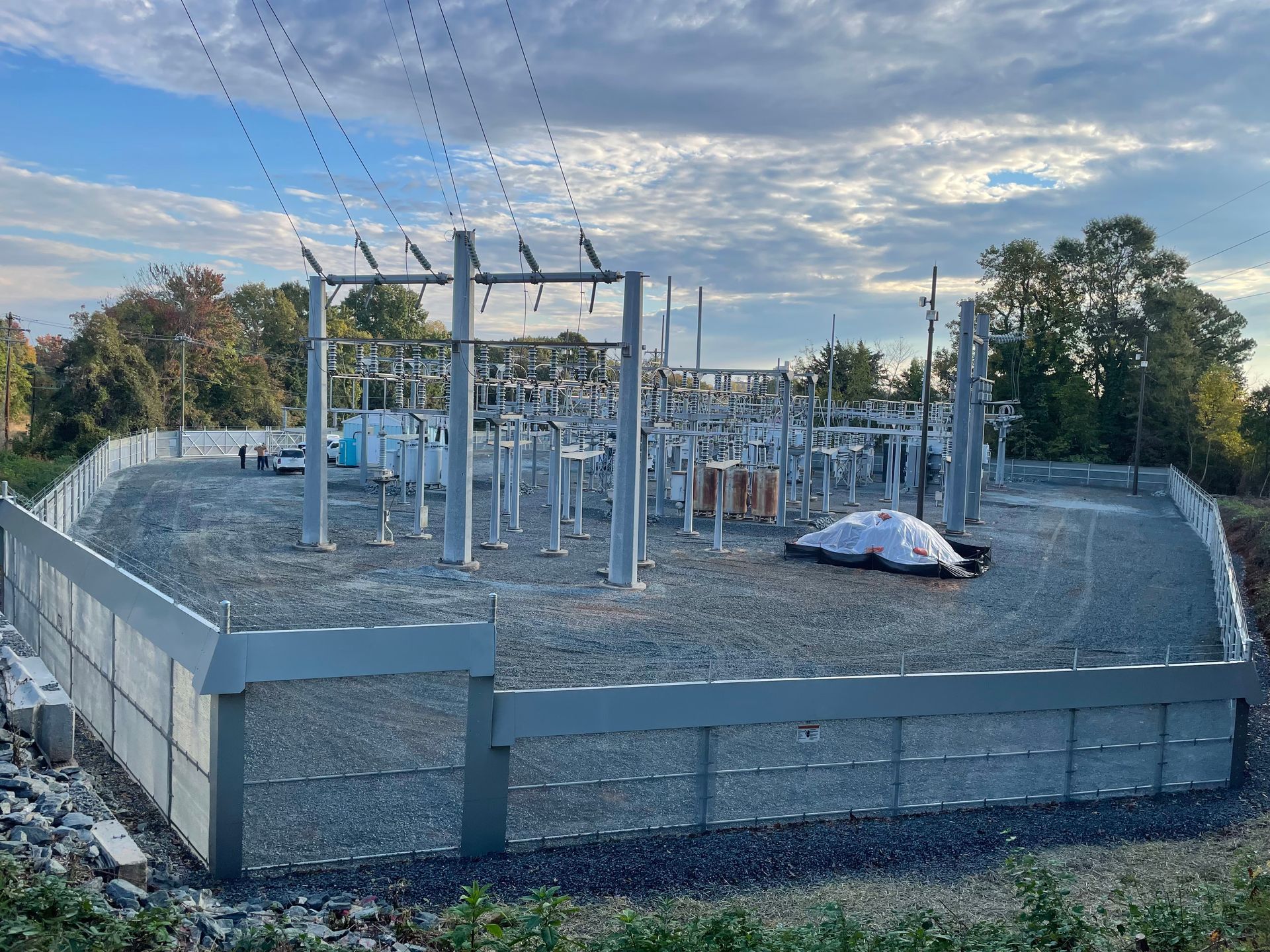 Electrical substation with gray fence and gravel, under a cloudy sky.