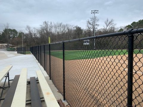 Chain-link fence borders a baseball field with a tan infield, green outfield, and bleachers on the left.