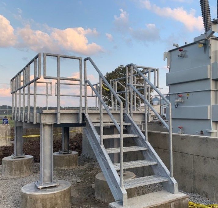 Steel platform with stairs next to electrical equipment; outdoor setting, blue sky.