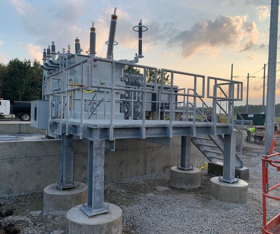 Electrical transformer with metal platform and stairs, set on concrete piers, outdoors.