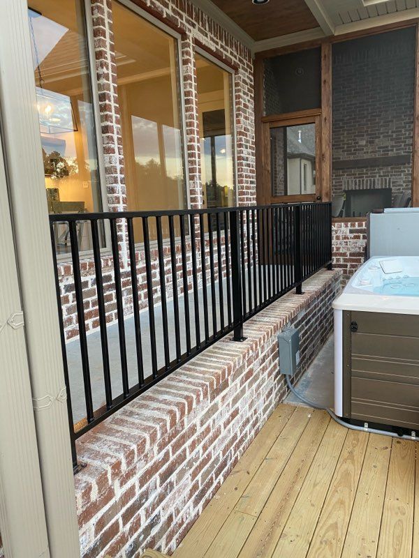Black metal railing on a brick wall, next to a wood deck and a hot tub.
