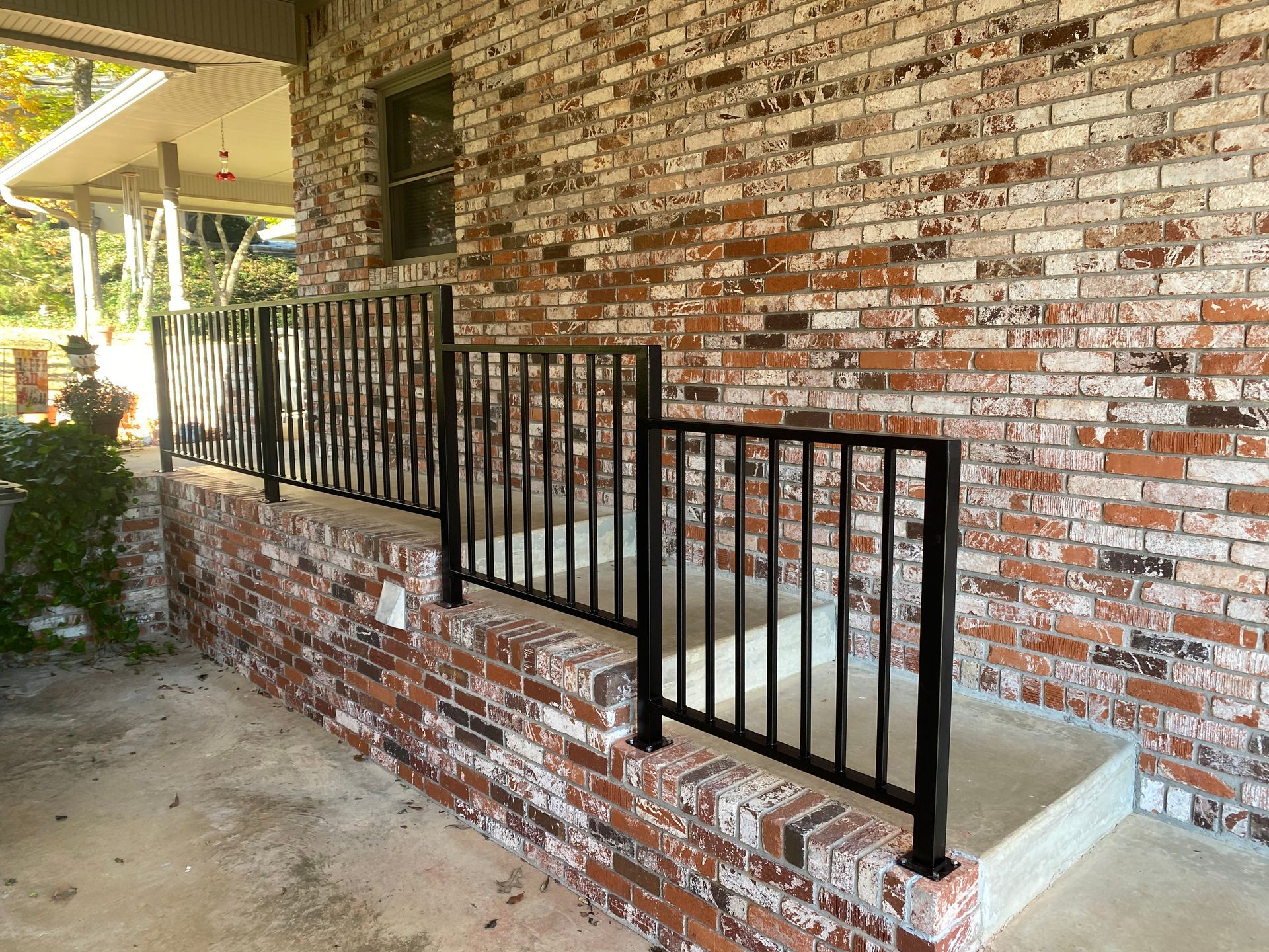 Black metal railing along a brick wall, part of a porch or walkway.