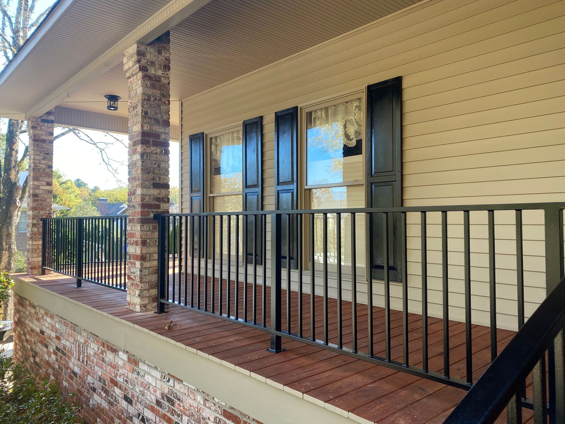 Exterior of a house with a porch. Brick and black railing, beige siding, black shutters.