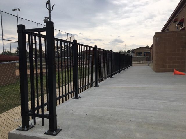 Black metal fence along a concrete walkway next to a building on a cloudy day.