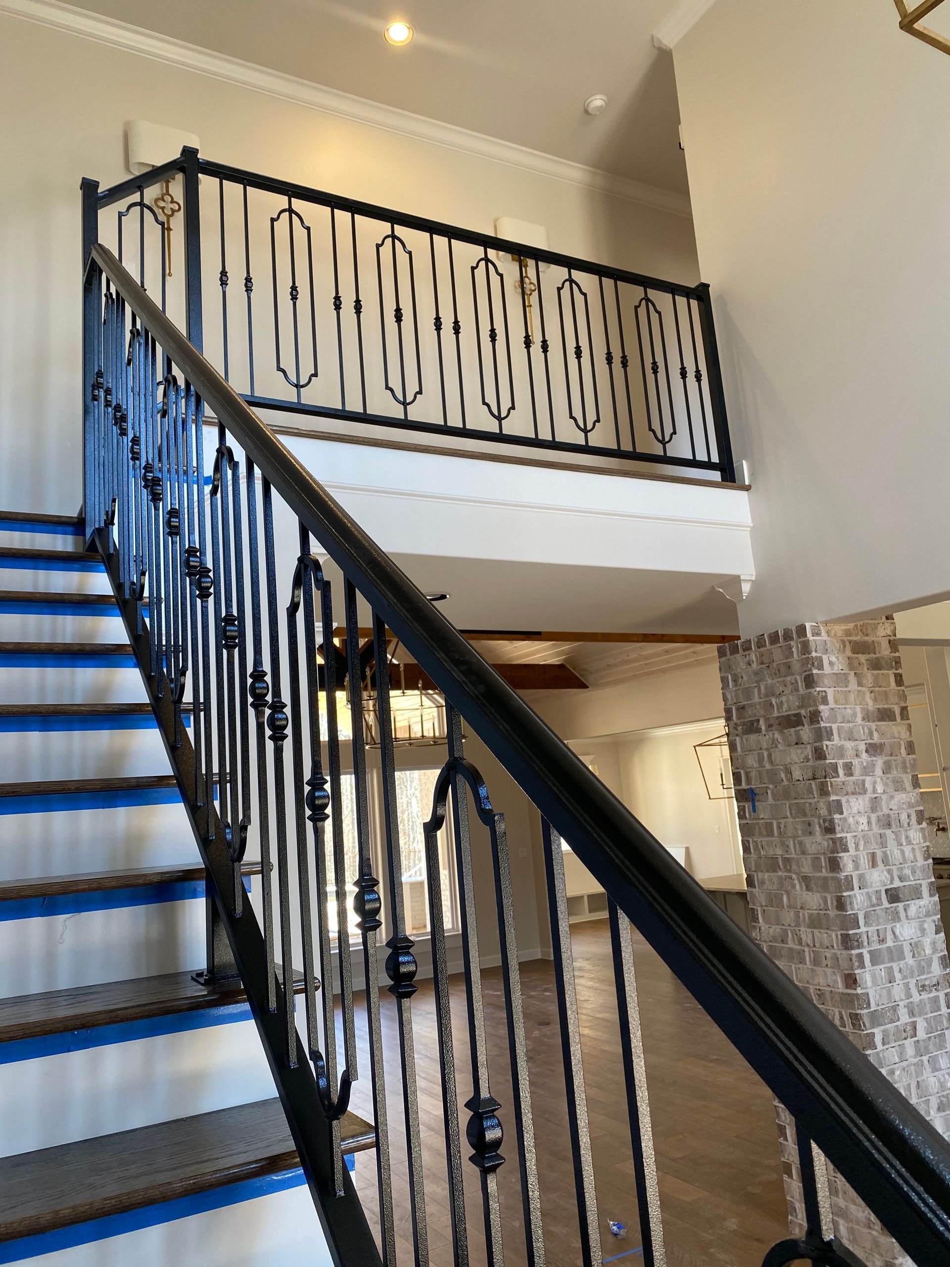 Black iron staircase railing with intricate design, leading to a second-floor balcony. Interior view.