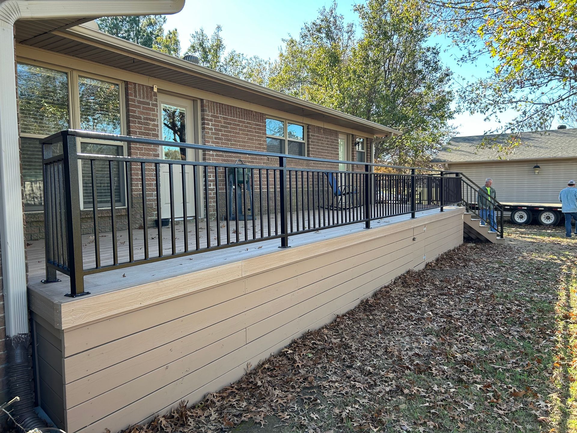 Raised deck with black railing and beige skirting beside a brick house, covered in fallen leaves.
