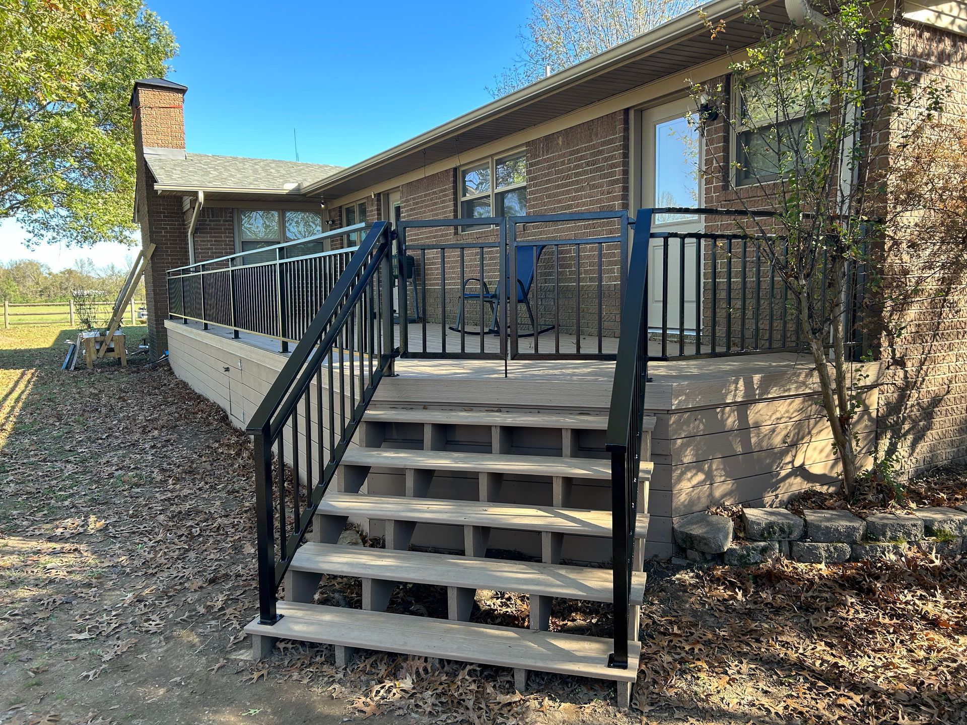 Brick house porch with black railings and front steps surrounded by trees and fallen leaves
