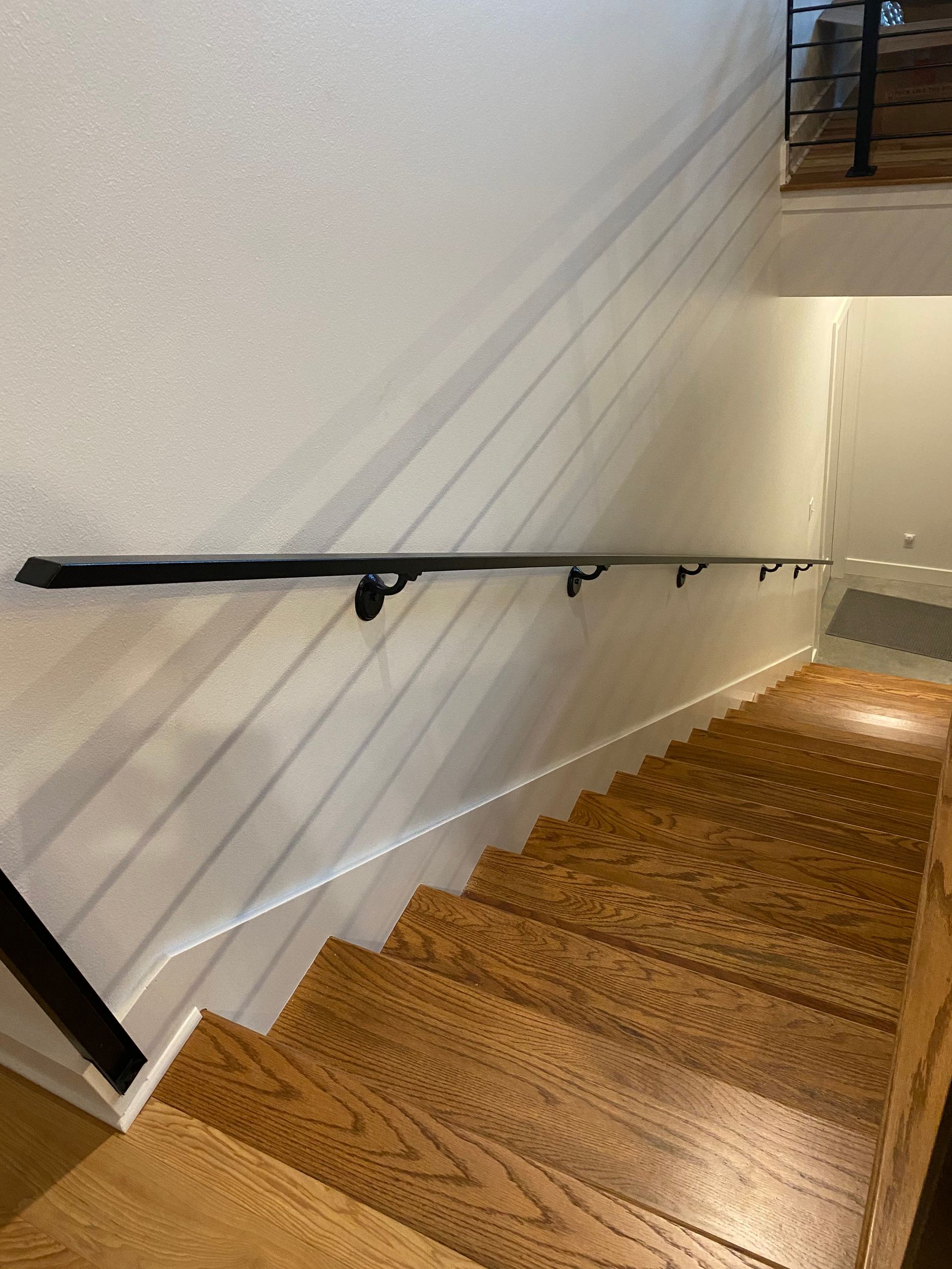 Wooden staircase with a black handrail on a white wall.