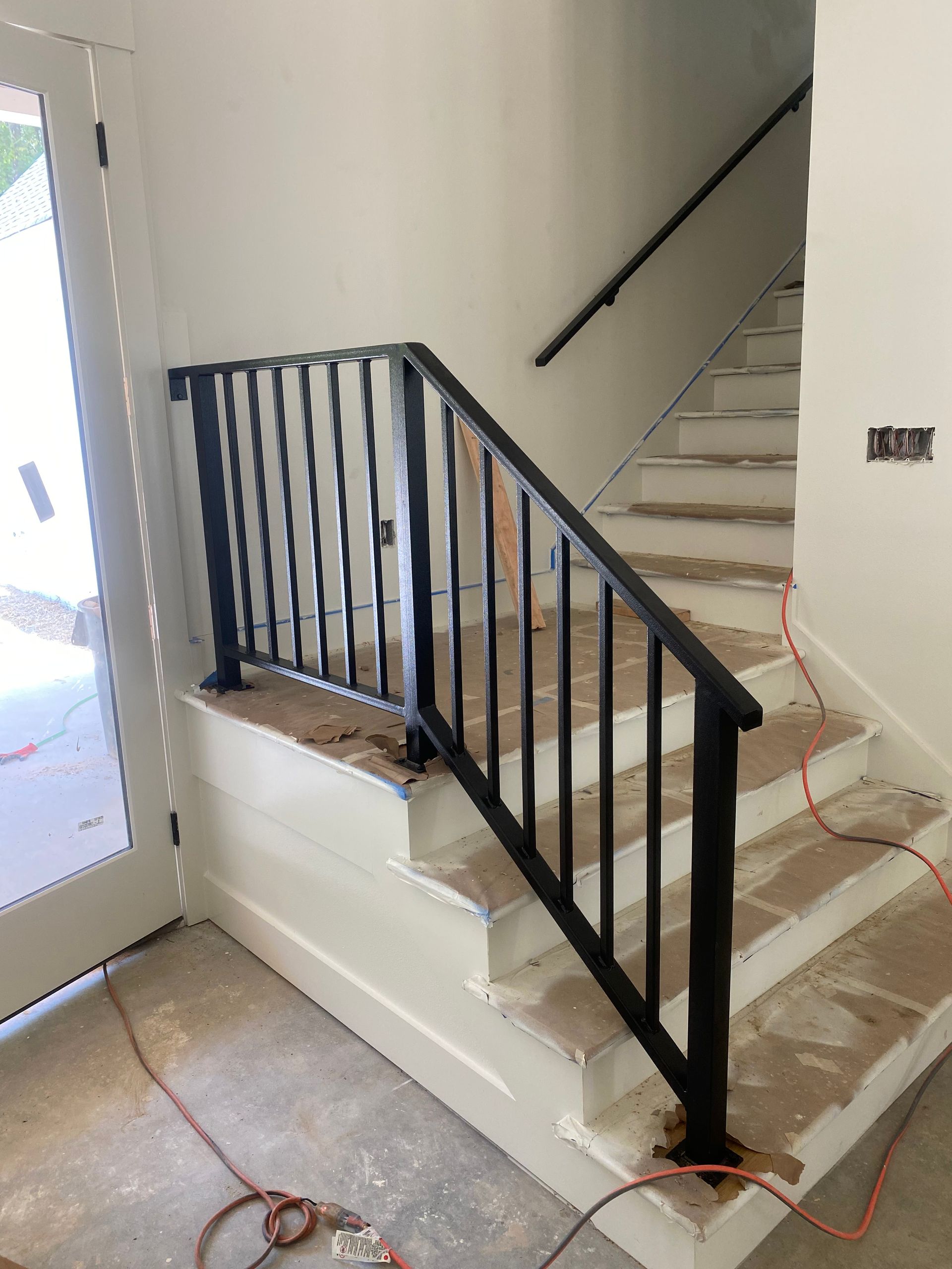Black metal stair railing with vertical bars on white stairs and wall.