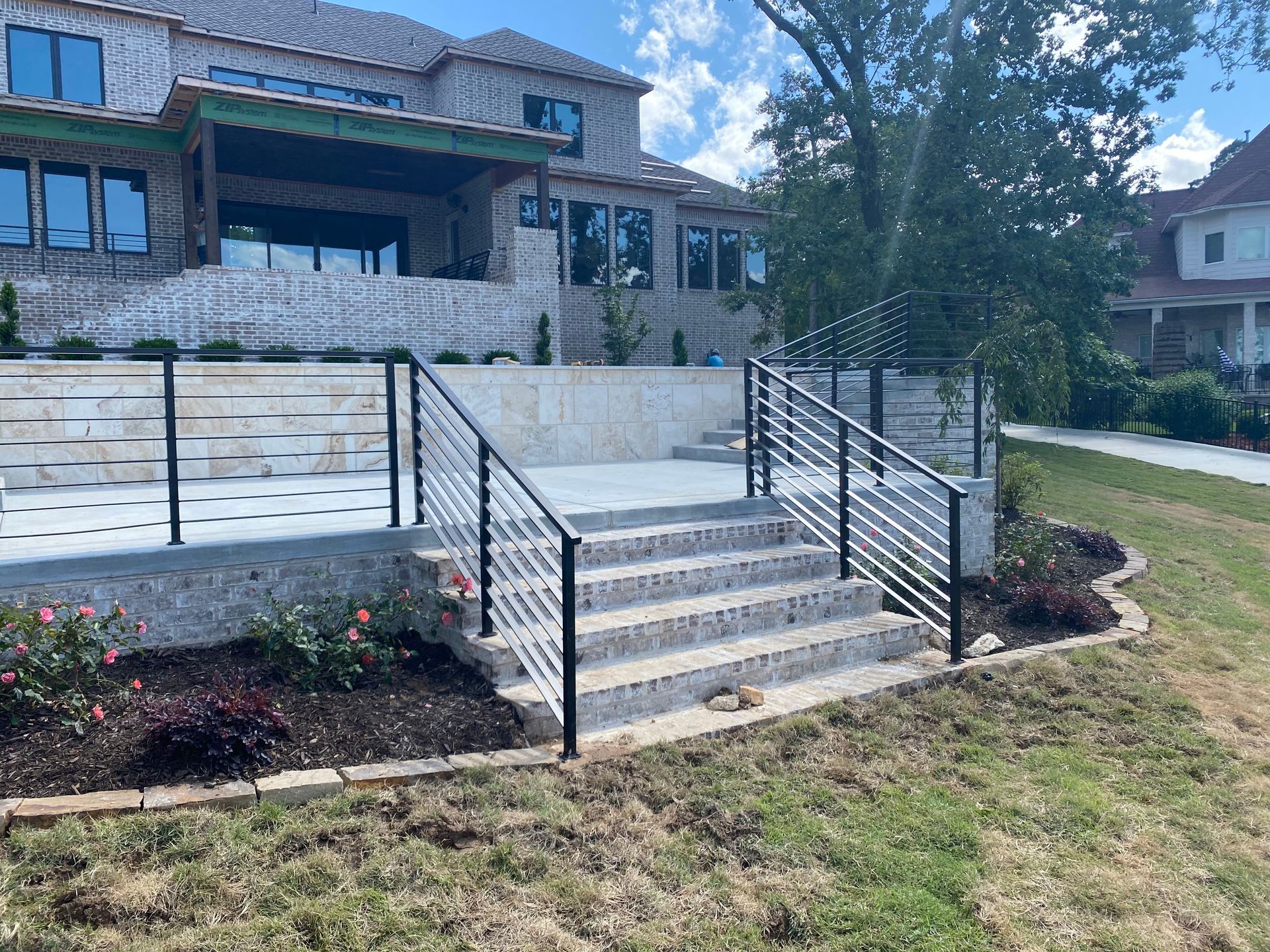 Stone house front entrance with concrete steps, black railings, and landscaped yard.