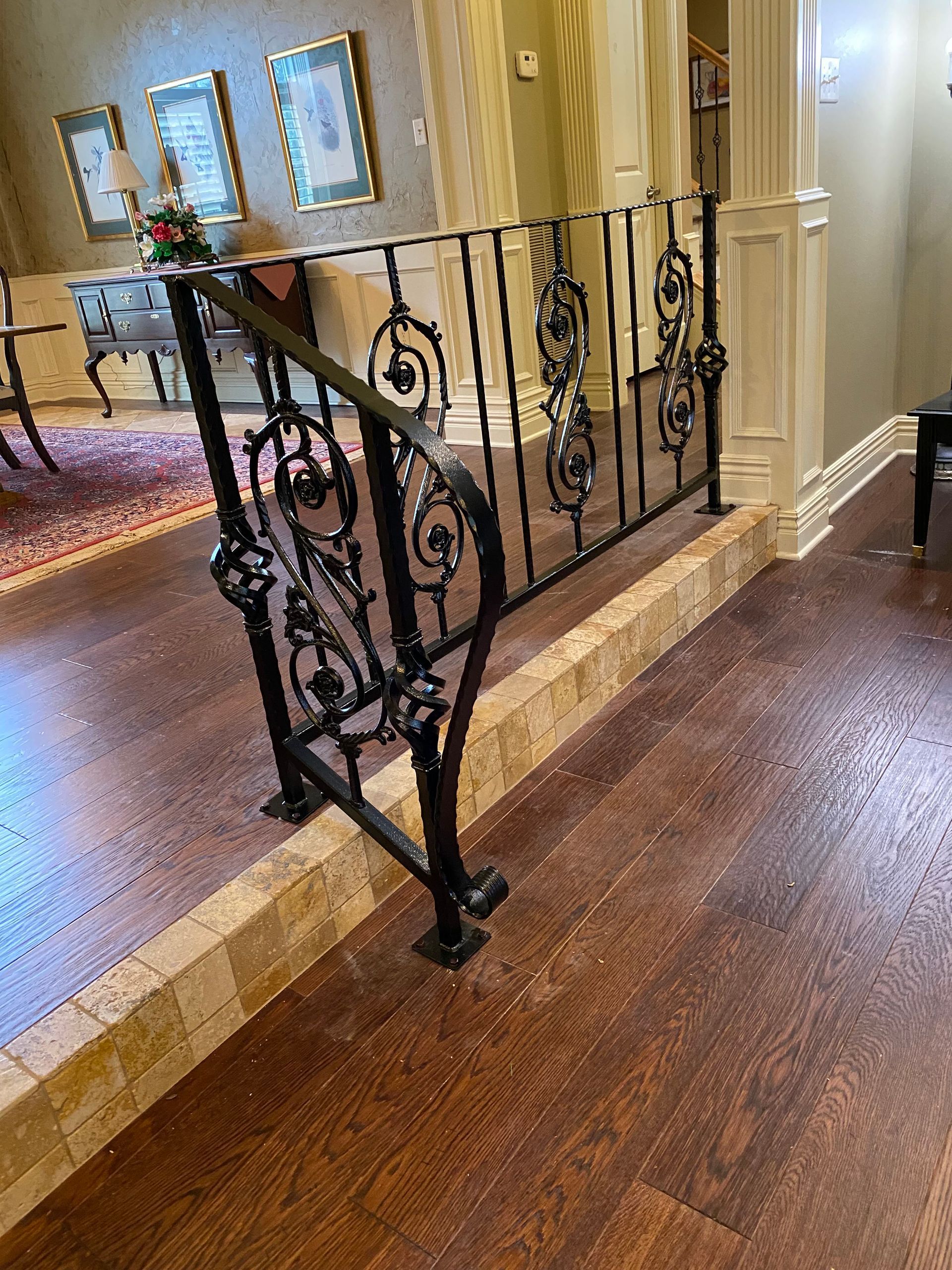 Black wrought-iron railing on a tiled step, adjacent to dark wood flooring in a building's interior.