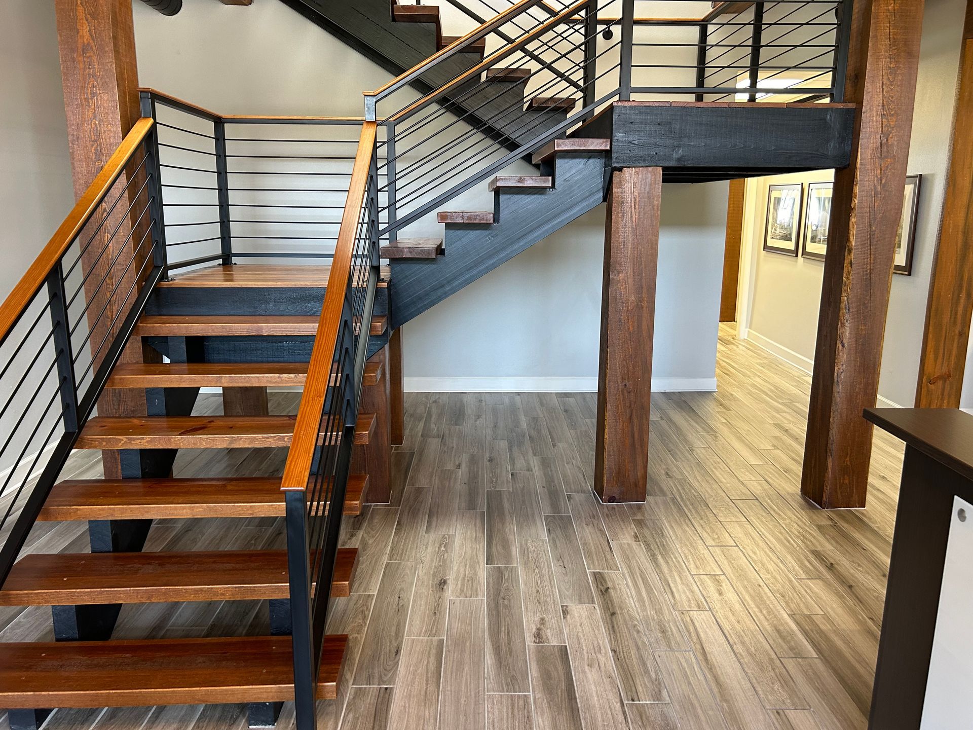 Wooden staircase with black metal railings and wood-look flooring in a building lobby.