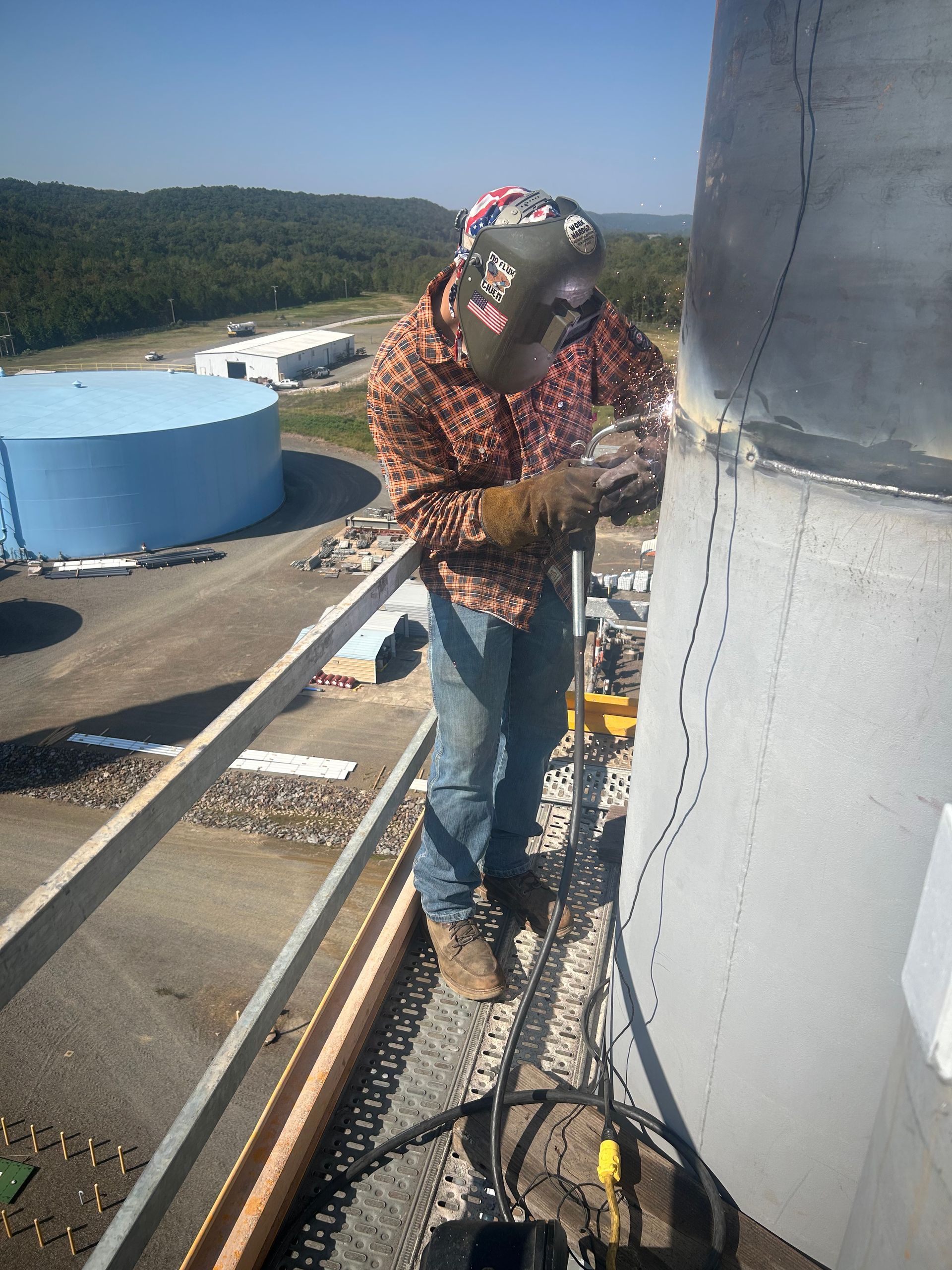 Welder on industrial structure. Wearing safety gear. Outdoors on sunny day.