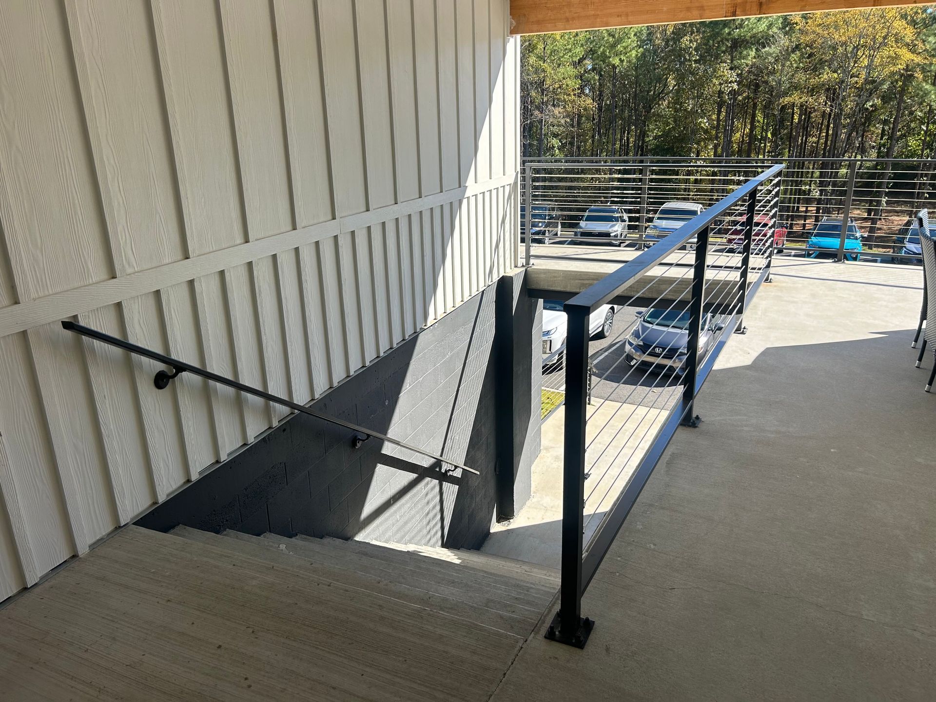 Outdoor ramp with black handrails beside a light-colored building and concrete walkway