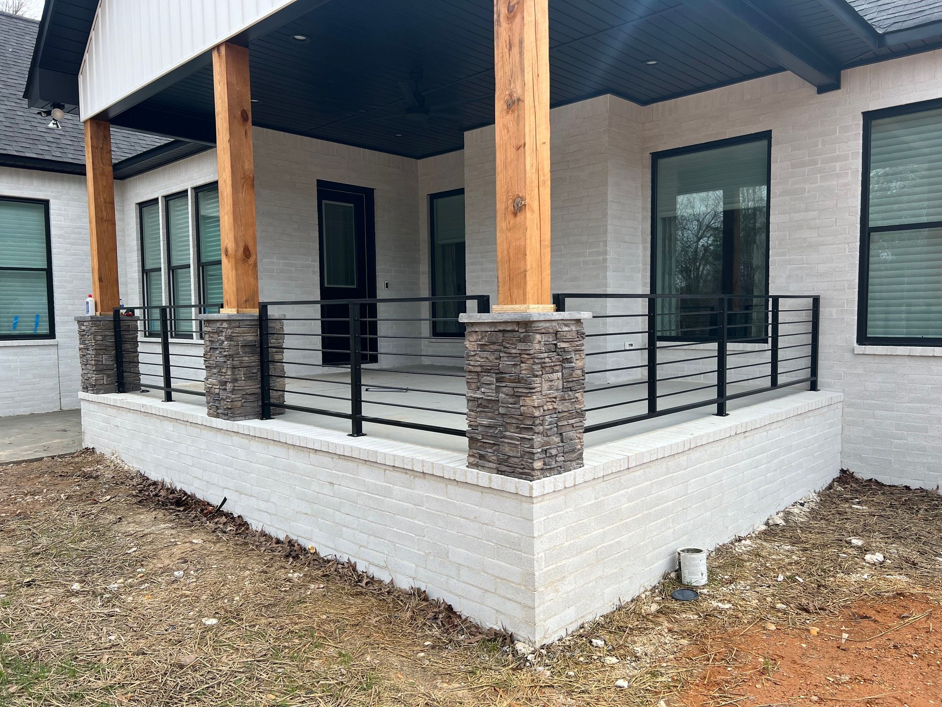 Covered porch with black railings, stone columns, and white brick exterior on a modern house