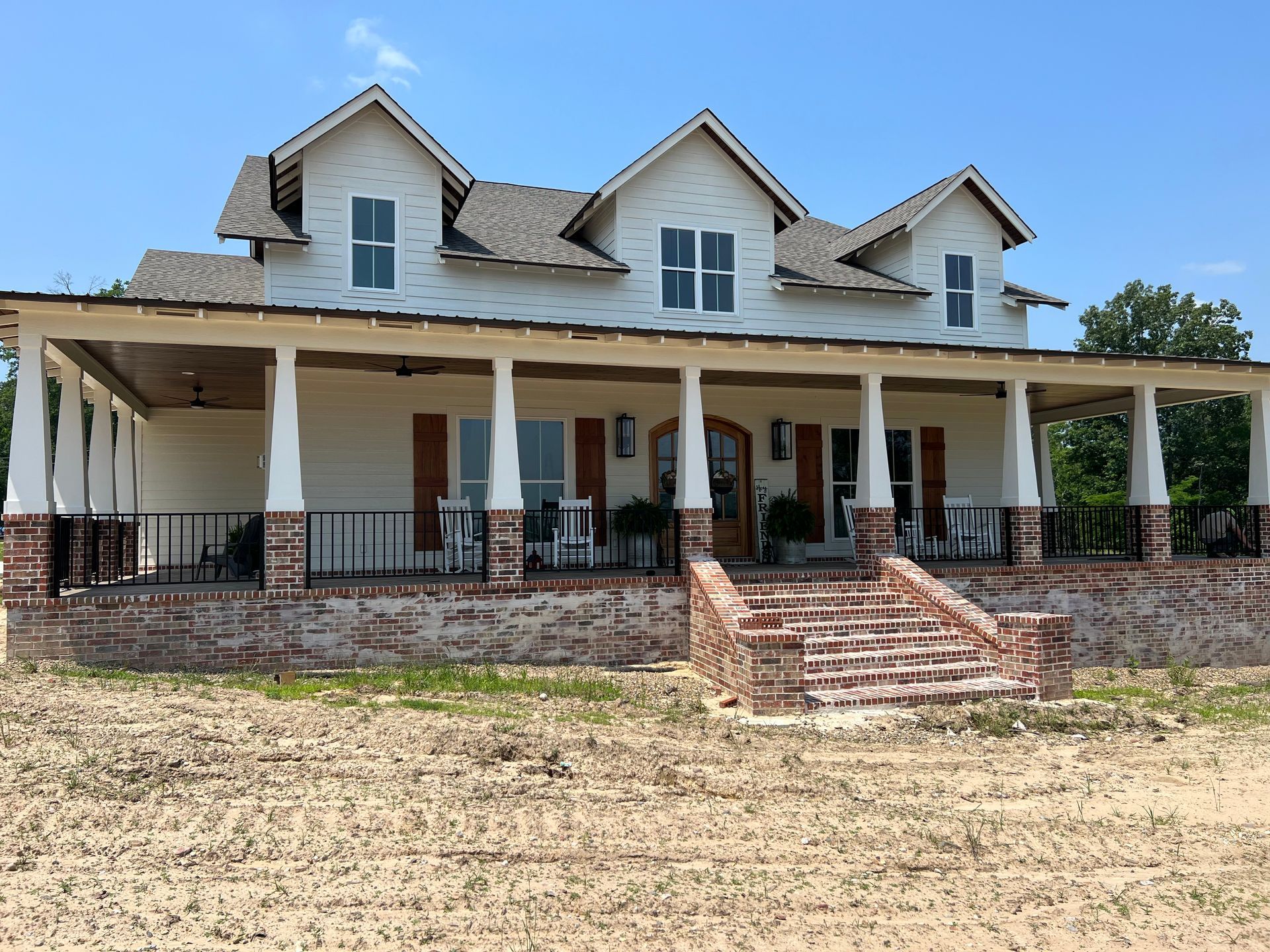 Large white farmhouse with a wraparound porch and brick steps on a sunny day