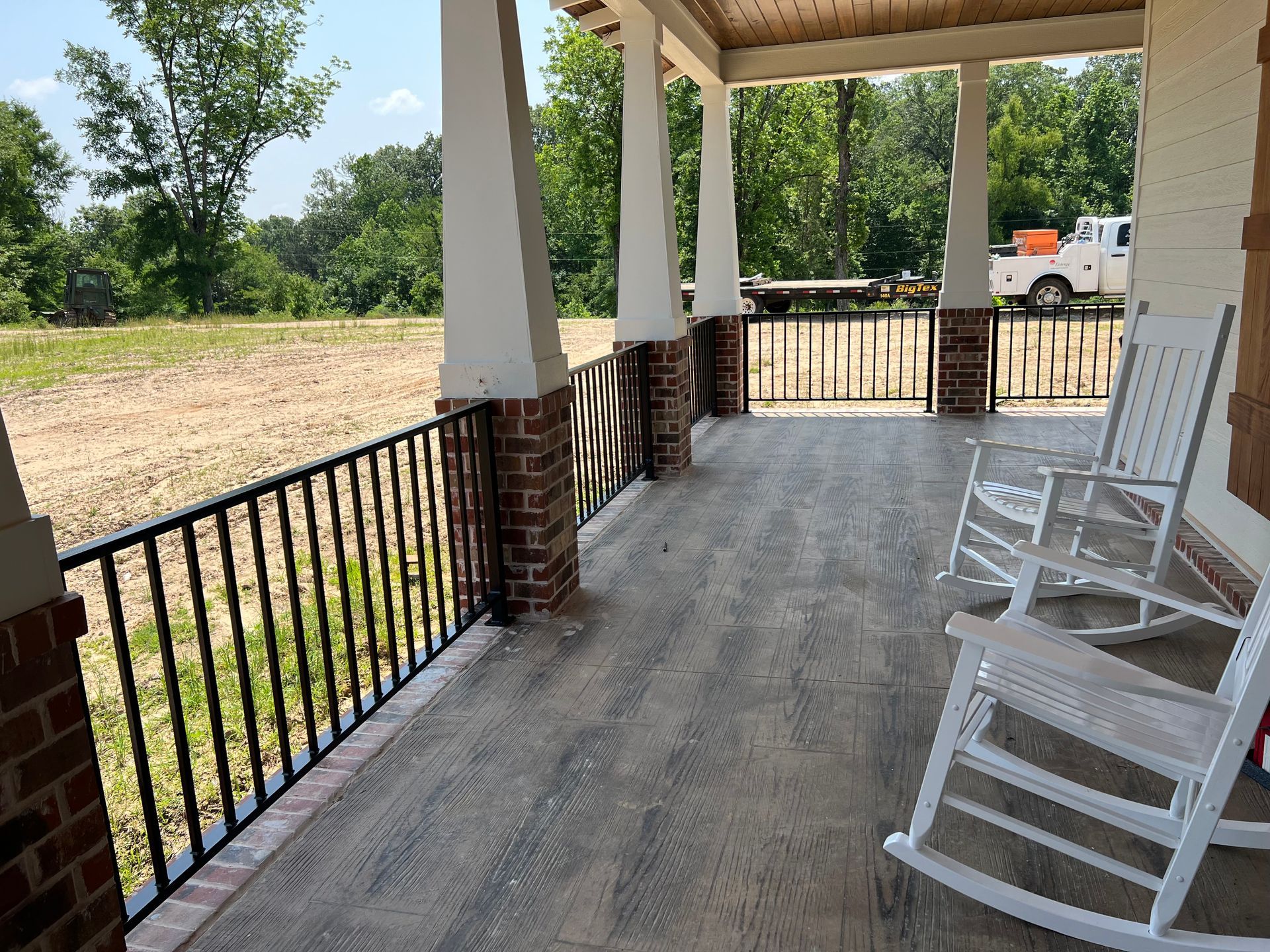 Porch with white rocking chairs, brick columns, black railing, and open field.