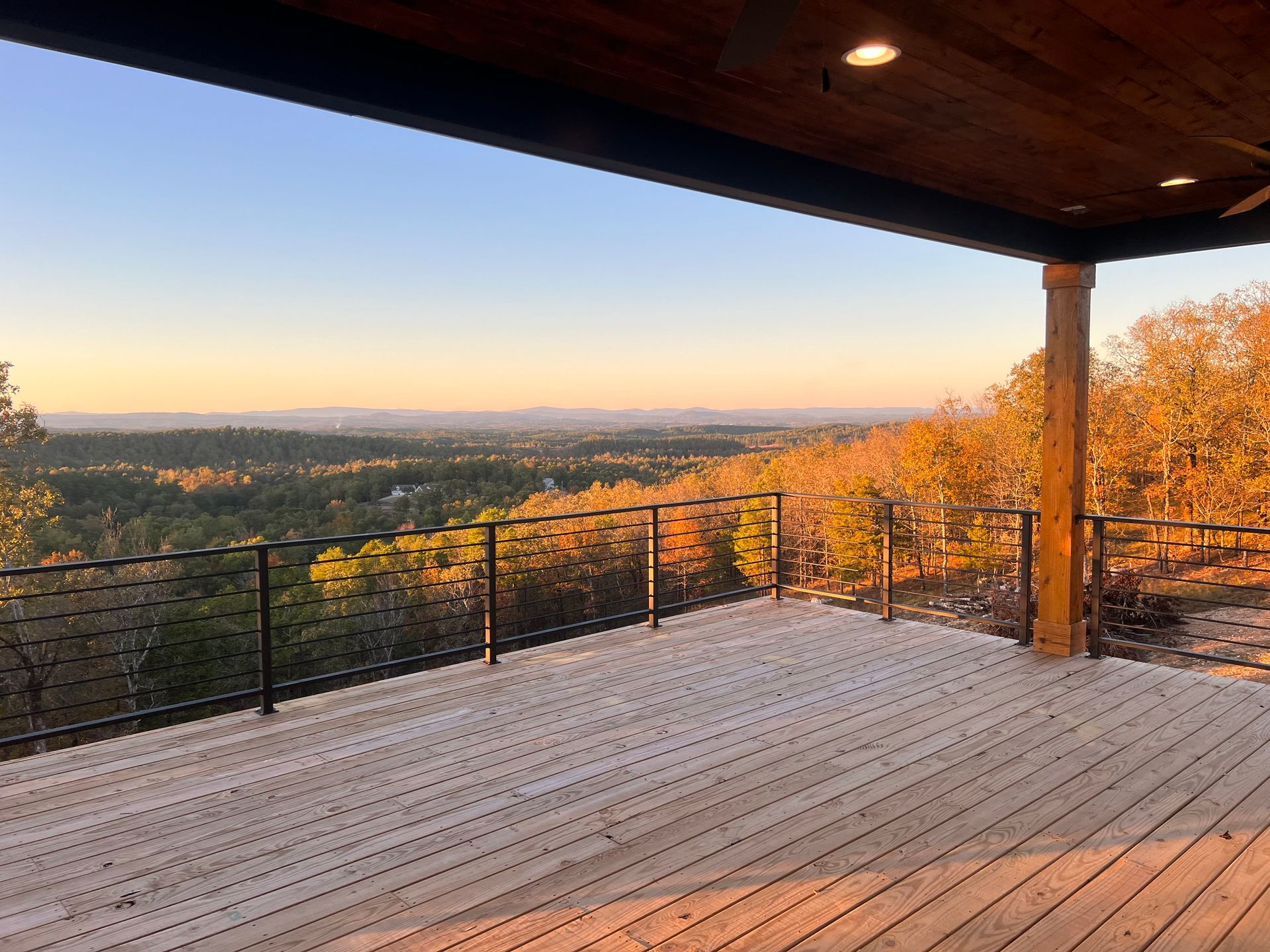 Wooden deck with a scenic view of a forest and mountains at sunset.