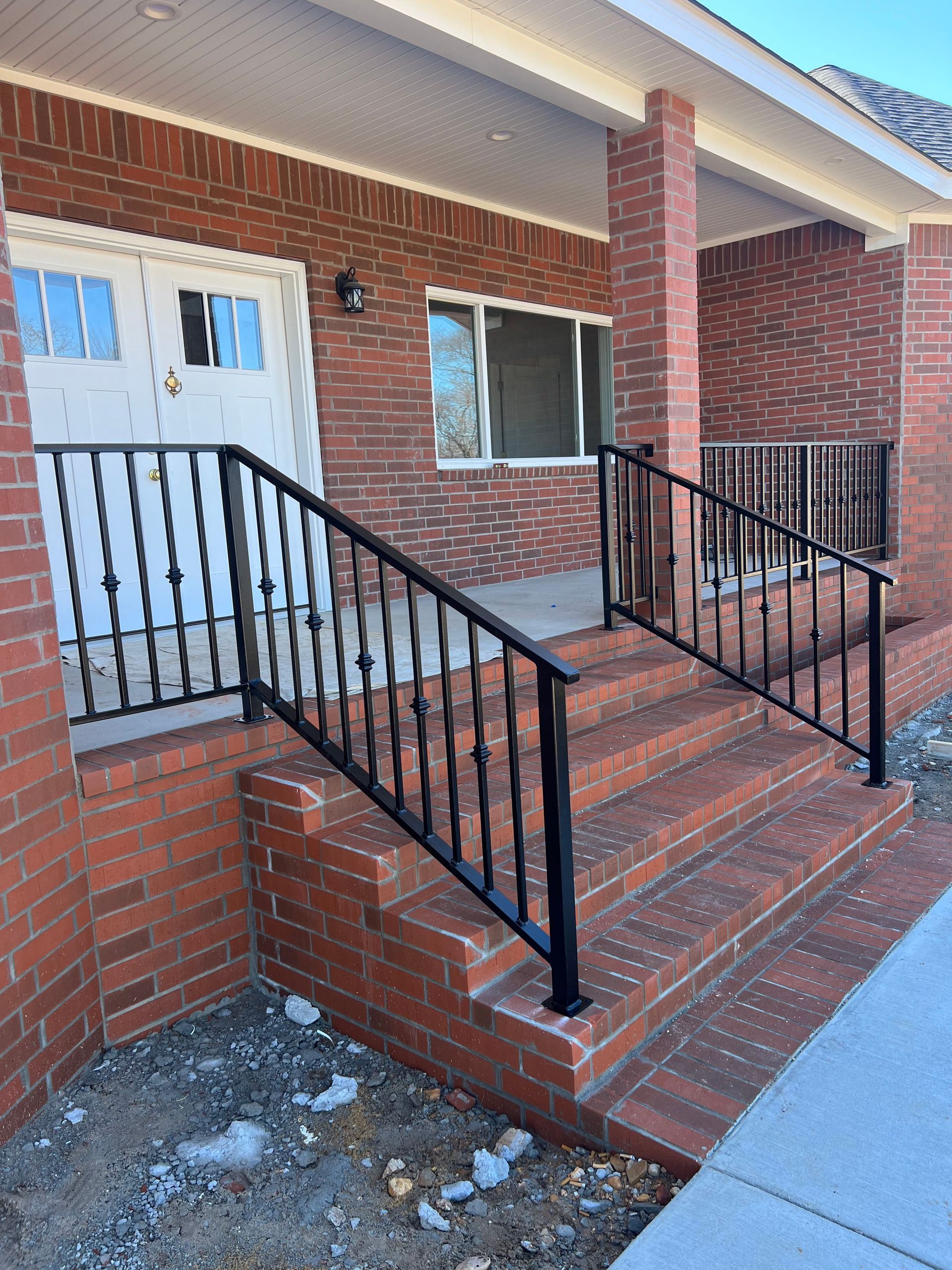 Brick house exterior with steps and black metal handrails. White door and window visible.