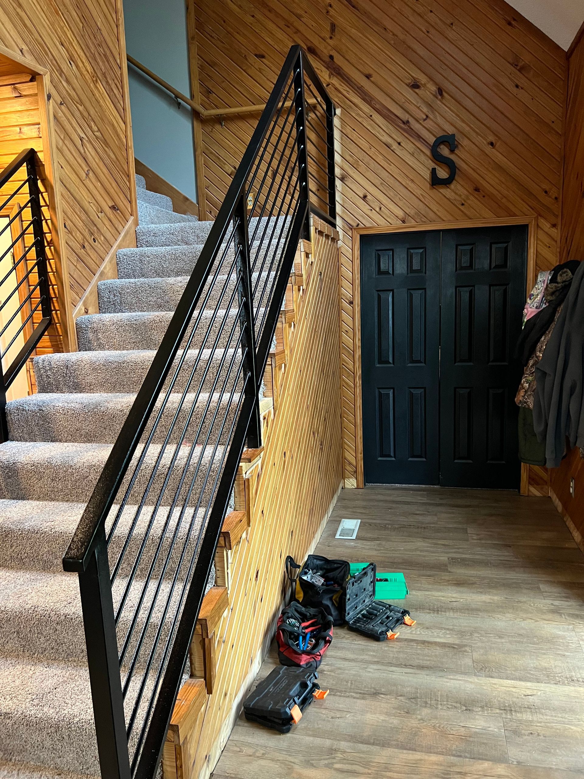 Staircase with black railing, light carpet, and wood-paneled walls, leading up to a door and landing.