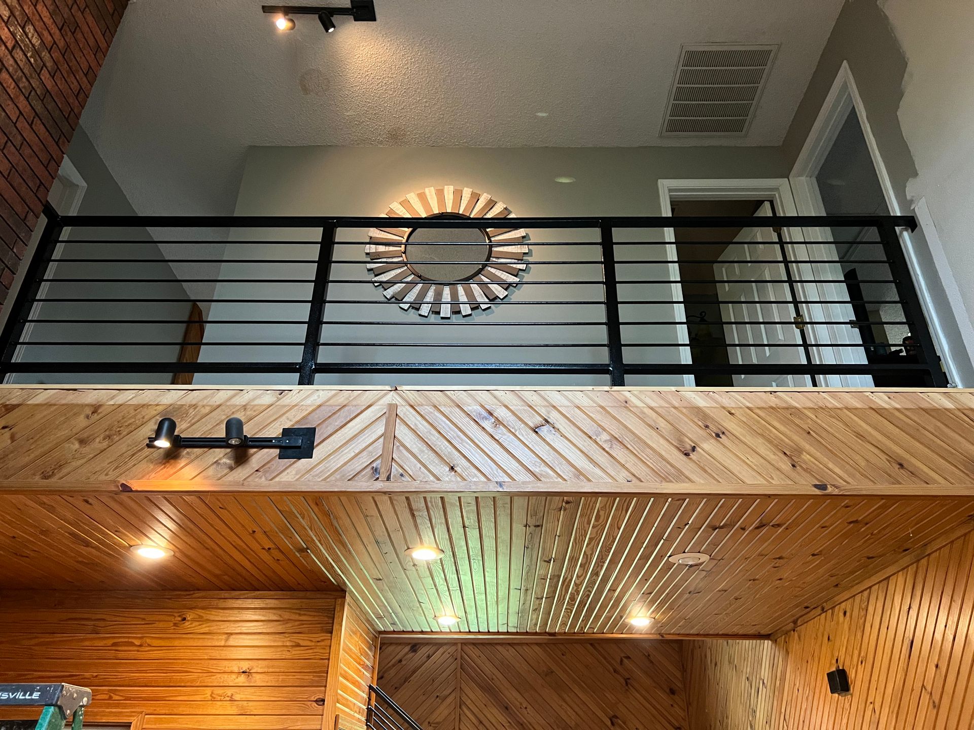 Interior view: wooden mezzanine with black railing, circular mirror, and recessed lighting.