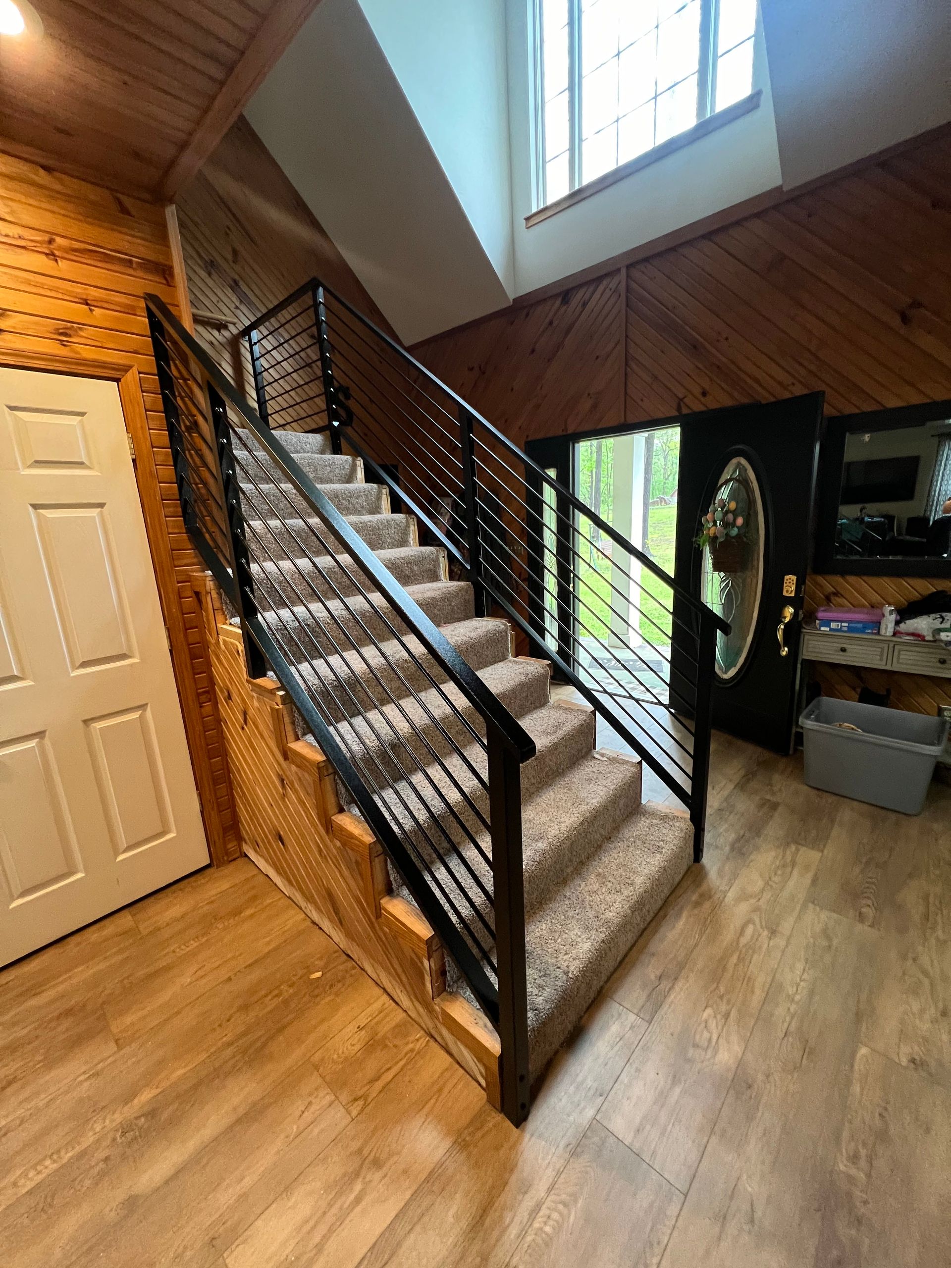 Staircase with black metal railing, carpeted steps, and wood paneling walls. Door to the side.