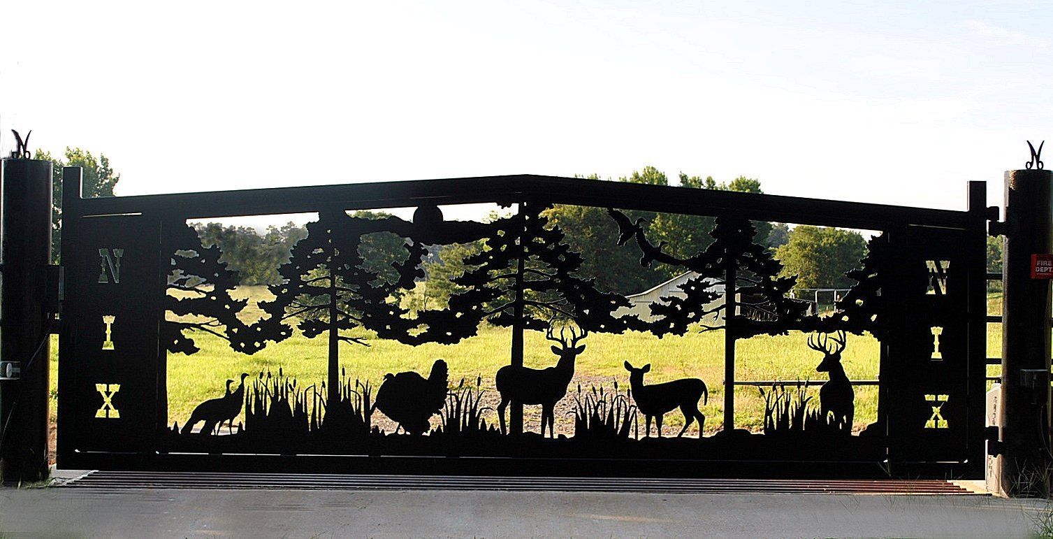 Black metal gate with forest scene silhouette: deer, turkey, trees, set in grassy field.