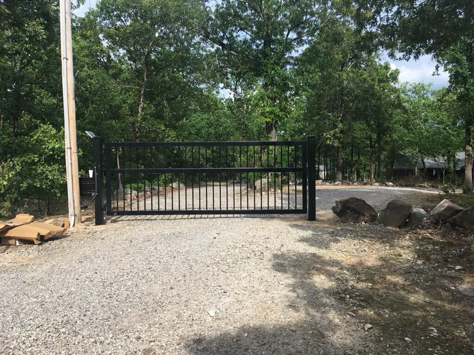 Black metal gate on a gravel driveway leading into a wooded area.