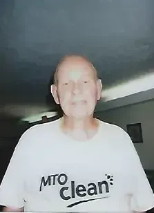 Person wearing a white “MTO Clean” shirt standing indoors in a dim room.