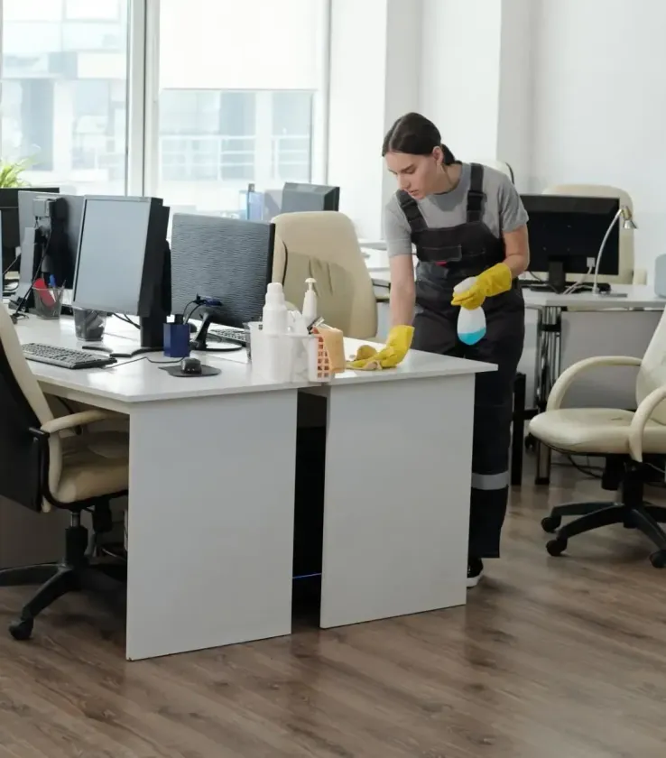 Cleaner wiping an office desk with yellow gloves in a modern workspace